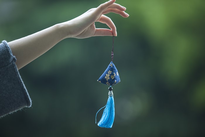 Hand holding a blue floral ornament with tassel