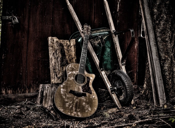 Acoustic guitar leaning against a weathered wooden wall and wheelbarrow