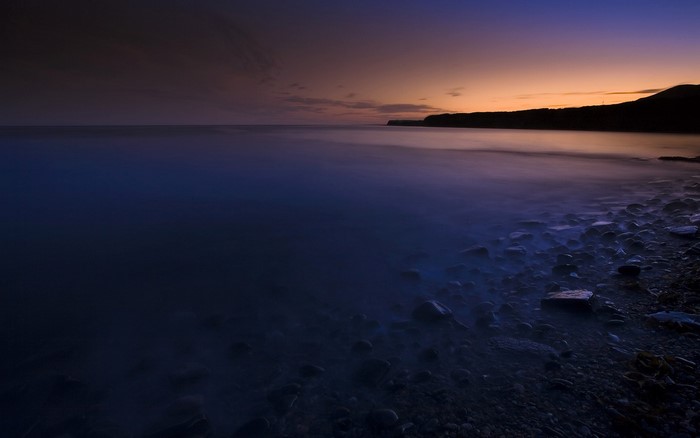 Dark beach at dawn with calm ocean and rocky shore