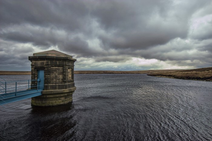 Reservoir tower with blue door and bridge under cloudy sky