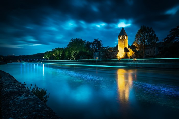 Night view of a river with light trails and a church tower in Lyon, France