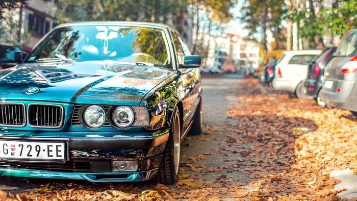 Teal BMW E34 parked on a street with fallen leaves