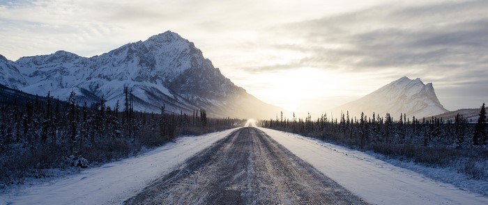 Snowy mountain road with sun and trees