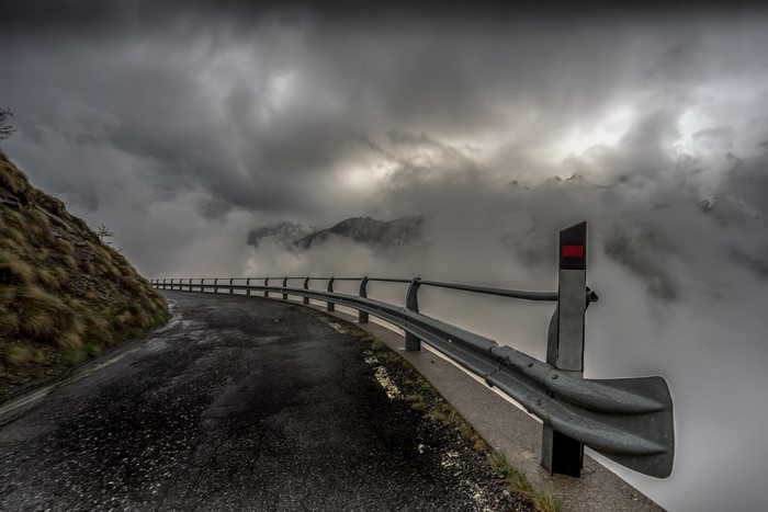 Winding mountain road with guardrail and clouds
