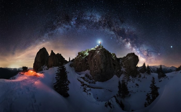 Man with headlamp on snowy mountain peak under Milky Way