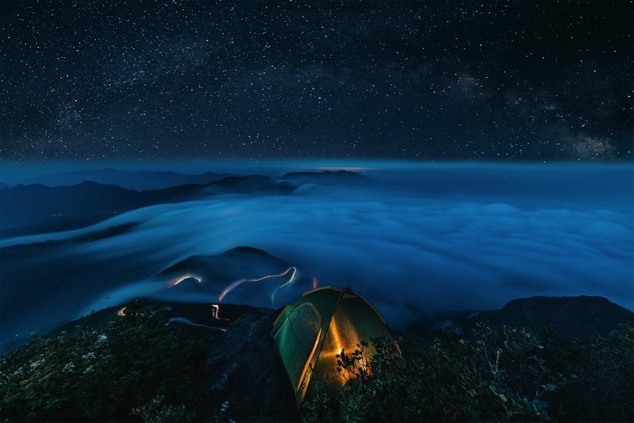 Tent under starry sky above sea of clouds