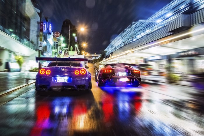 Two sports cars racing at night on a wet city street