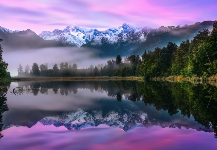 Misty mountains reflected in a purple lake at sunrise