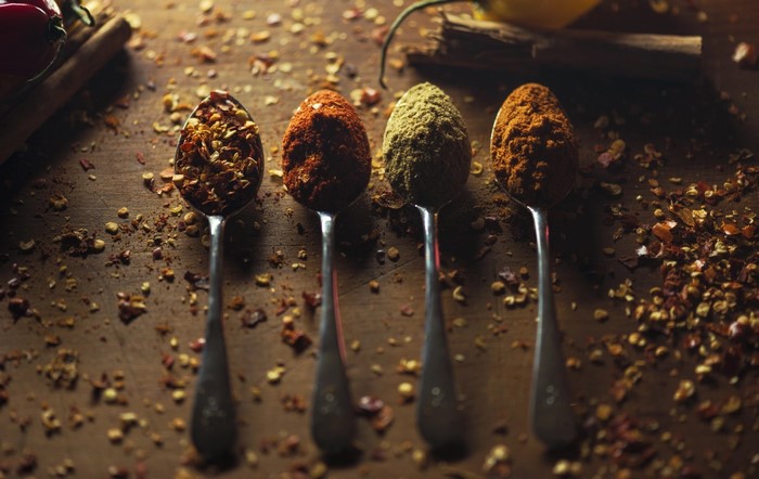 Four spoons filled with colorful spices on a wooden surface