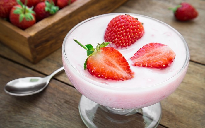 Strawberries and yogurt in a glass bowl with a spoon