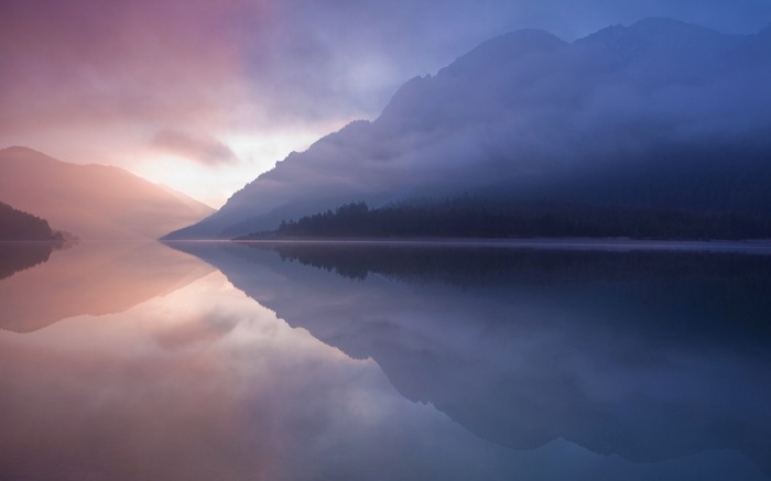 Misty mountains reflected in a calm lake at sunrise