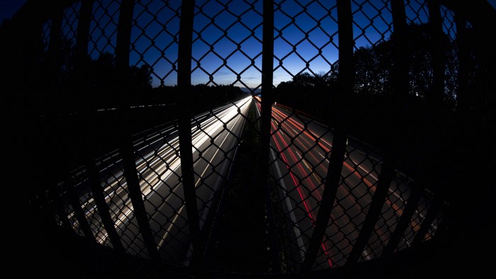 Long exposure of highway traffic at dusk through a fence