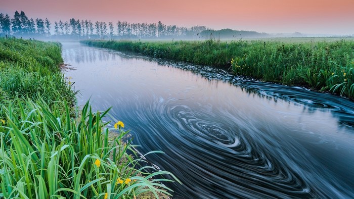 River with swirling water and green grass at sunrise