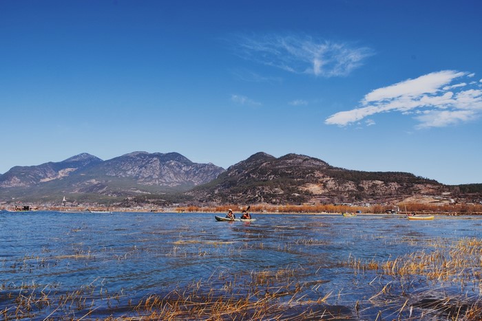 Kayakers on a lake with mountains and a village in Yunnan, China