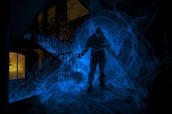 Man surrounded by blue light in a dark, ruined building