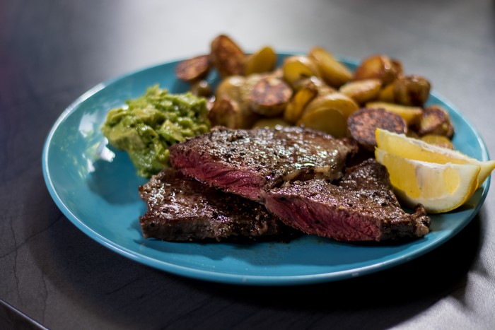 Steak with potatoes, guacamole, and lemon