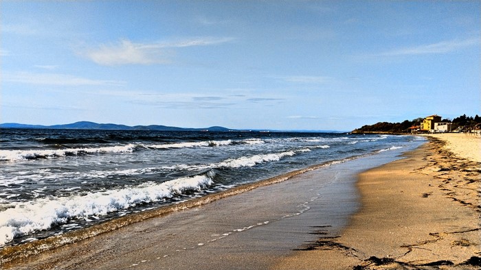 Waves crashing on a sandy beach with buildings in the distance