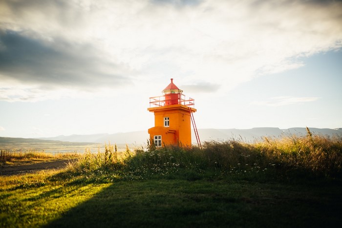 Orange lighthouse on a grassy hill at sunset