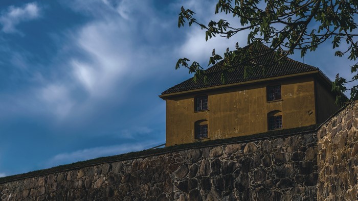 Old yellow building on stone wall under blue sky