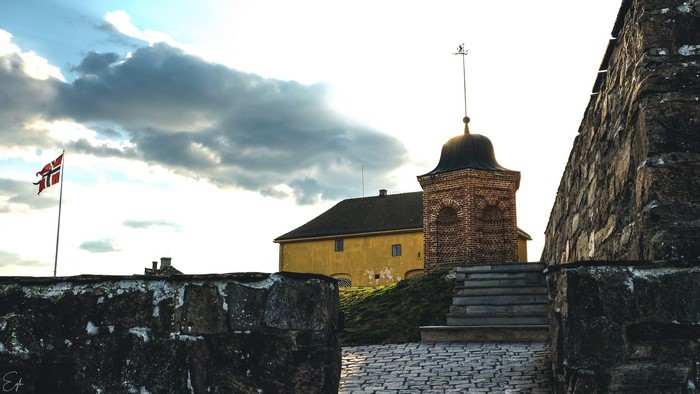Norway flag near old brick tower and yellow building