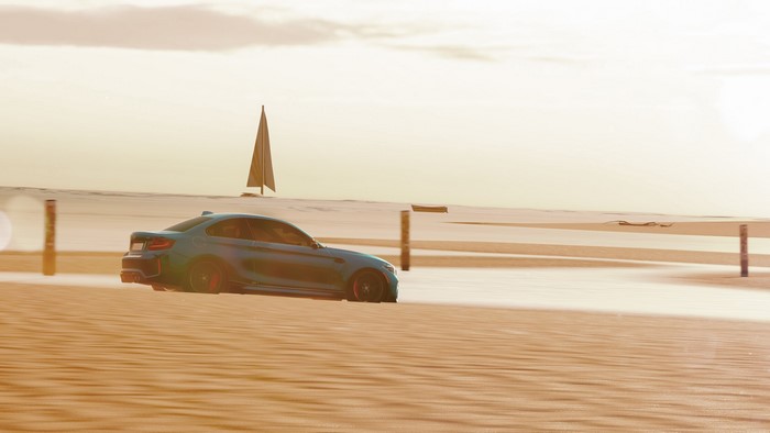 Blue BMW M2 driving on a sandy beach with a sailboat