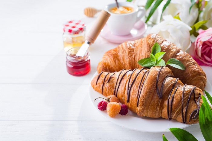 Croissants with jam, honey, coffee, and flowers