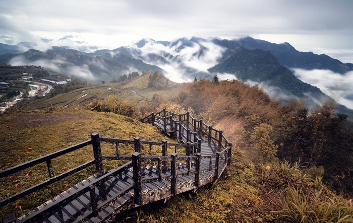 Wooden walkway overlooking misty mountains and tea plantations