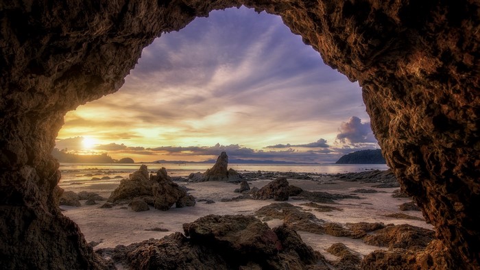 Cave entrance overlooking a rocky beach at sunset