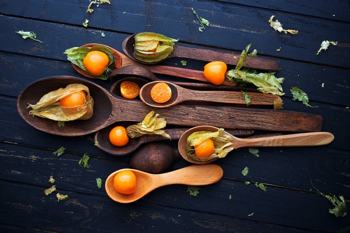 Physalis fruits in wooden spoons on a dark surface