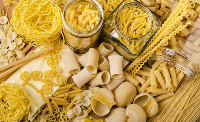 Assortment of dry pasta types in jars and scattered