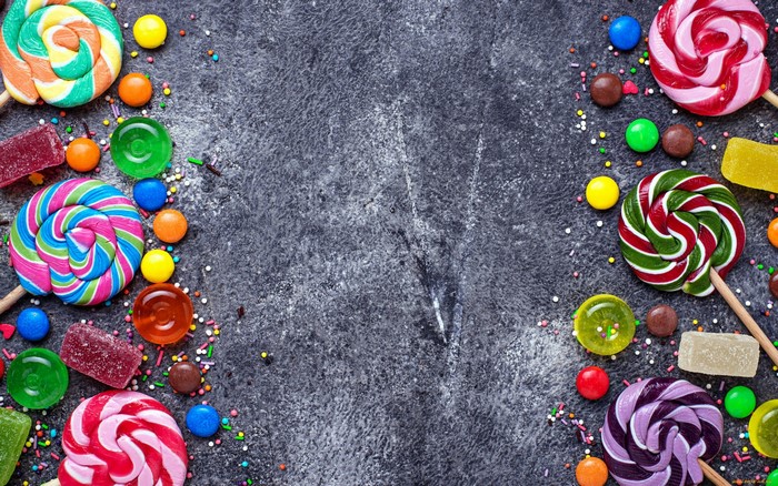 Assortment of colorful candies and lollipops on a dark textured surface