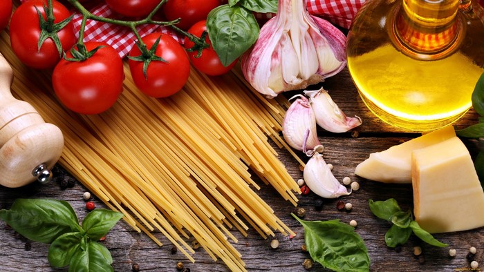 Spaghetti, tomatoes, garlic, olive oil, and cheese on a wooden surface