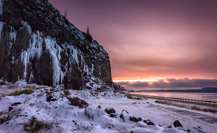 Winter scene with icy cliff and sunset over water