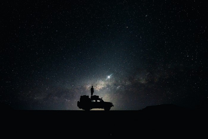 Silhouette of a person on a car under the stars