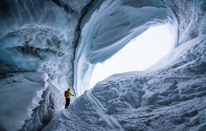 Person in ice cave with backpack and ski poles