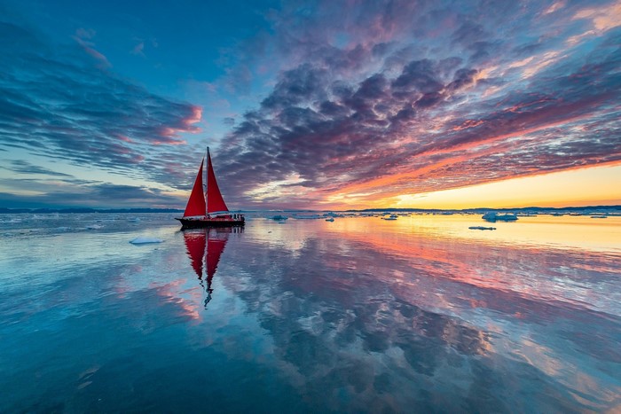 Sailboat with red sails on calm water at sunset