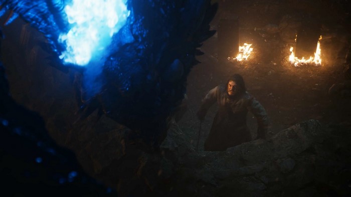 Jon Snow facing a dragon breathing blue fire in a cave