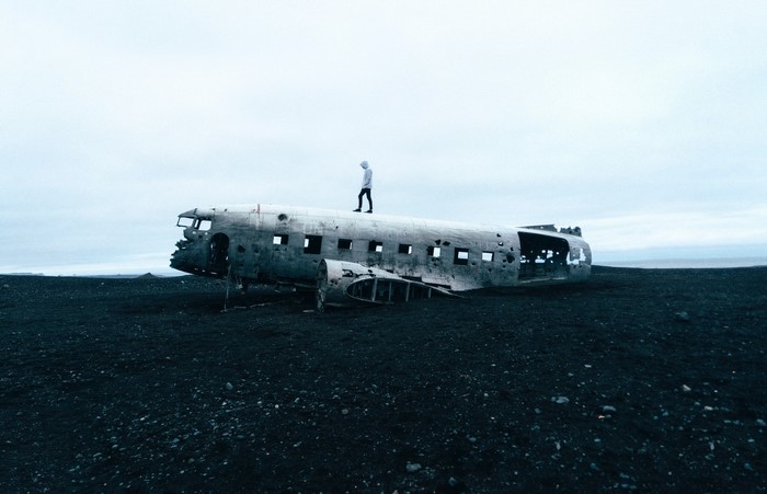 Person standing on a plane wreck on a black sand beach