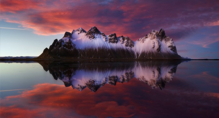 Snow-capped mountains reflected in calm water at sunset
