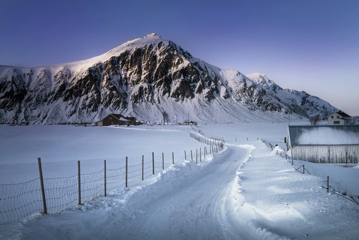 Snowy road leading to mountains with houses in winter