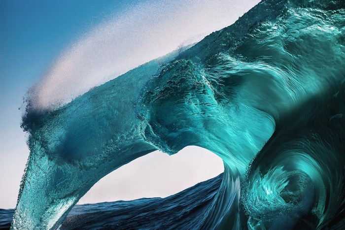 Turquoise wave crashing with spray against blue sky