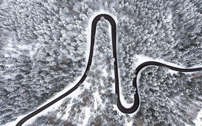 Aerial view of a winding road through a snow-covered forest