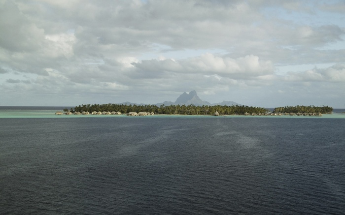 Overwater bungalows on a tropical island with mountains in the background