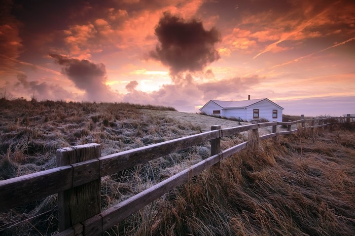 White house on a hill with a wooden fence at sunset