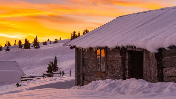Wooden cabin in snow during sunrise with icicles