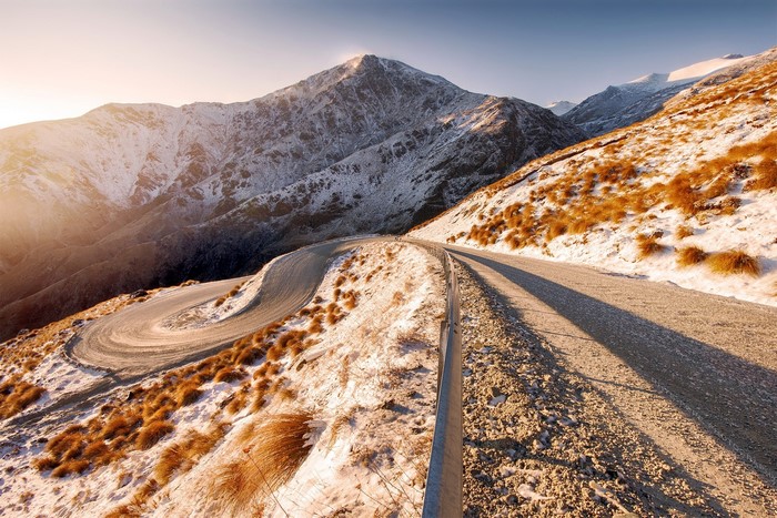 Winding mountain road with snow and dry grass