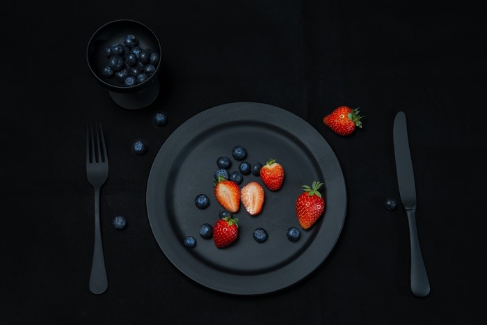 Black plate with strawberries and blueberries, fork and knife