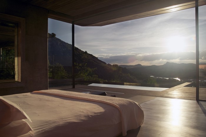 Bedroom with a view of mountains and a pool at sunset