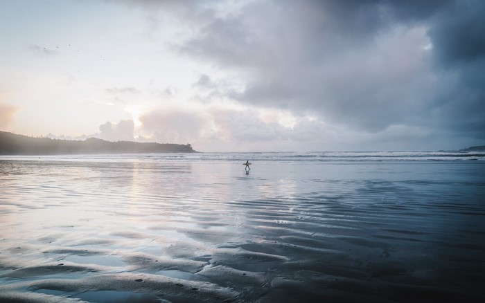 Surfer walking on a wet beach at sunset