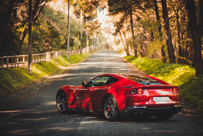 Red Ferrari driving on a tree-lined road